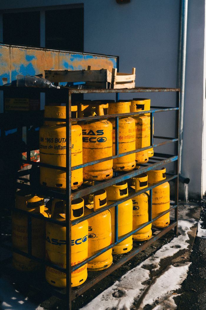 A row of yellow gas cylinders in a metal rack outside, against a wall.